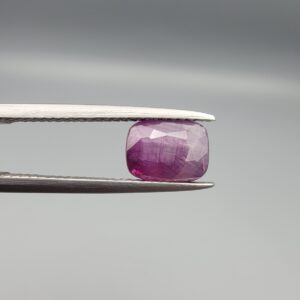 A rare 2.46-carat pinkish-red ruby from Mozambique featuring a faceted oval cut with distinctive natural internal silk patterns and small crystal inclusions, held in professional jeweler's tweezers.