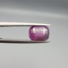 A rare 2.46-carat pinkish-red ruby from Mozambique featuring a faceted oval cut with distinctive natural internal silk patterns and small crystal inclusions, held in professional jeweler's tweezers.