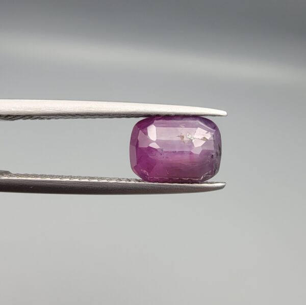 A rare 2.46-carat pinkish-red ruby from Mozambique featuring a faceted oval cut with distinctive natural internal silk patterns and small crystal inclusions, held in professional jeweler's tweezers.