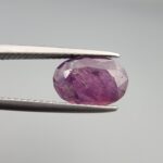 A substantial natural 2.41-carat pinkish-red ruby from Mozambique featuring a faceted oval cut with beautiful natural internal silk and crystalline inclusions, held in professional jeweler's tweezers.