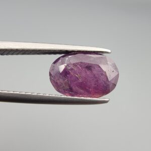 A substantial natural 2.41-carat pinkish-red ruby from Mozambique featuring a faceted oval cut with beautiful natural internal silk and crystalline inclusions, held in professional jeweler's tweezers.
