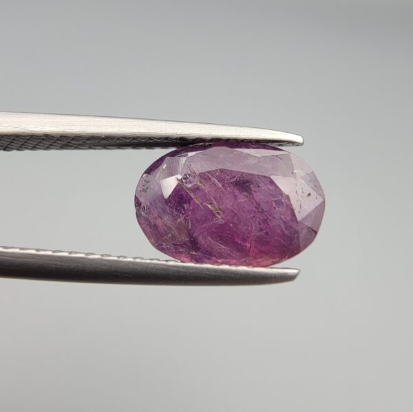 A substantial natural 2.41-carat pinkish-red ruby from Mozambique featuring a faceted oval cut with beautiful natural internal silk and crystalline inclusions, held in professional jeweler's tweezers.