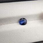 A natural 1.00-carat blue sapphire (Neelam) from Ceylon, Sri Lanka, featuring a faceted oval cut with a distinct cornflower blue saturation, held in professional jeweler's tweezers.
