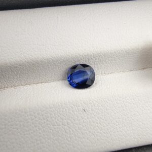 A natural 1.00-carat blue sapphire (Neelam) from Ceylon, Sri Lanka, featuring a faceted oval cut with a distinct cornflower blue saturation, held in professional jeweler's tweezers.