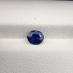 A natural 1.13-carat blue sapphire (Neelam) from Ceylon, Sri Lanka, featuring a faceted oval cut with strong cornflower blue saturation and exceptional clarity, held in professional jeweler's tweezers.
