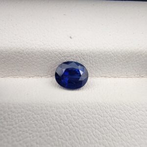 A natural 1.13-carat blue sapphire (Neelam) from Ceylon, Sri Lanka, featuring a faceted oval cut with strong cornflower blue saturation and exceptional clarity, held in professional jeweler's tweezers.