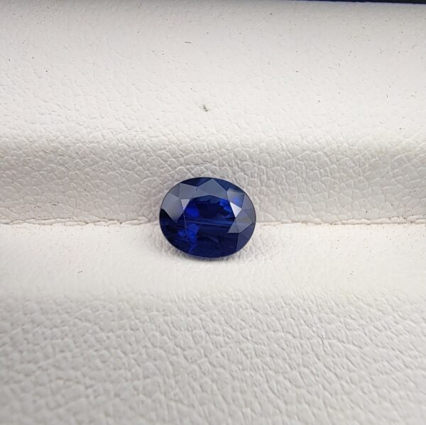 A natural 1.13-carat blue sapphire (Neelam) from Ceylon, Sri Lanka, featuring a faceted oval cut with strong cornflower blue saturation and exceptional clarity, held in professional jeweler's tweezers.