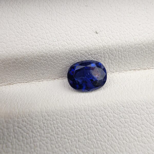 A natural 1.23-carat blue sapphire (Neelam) from Ceylon, Sri Lanka, featuring a faceted oval cut with vibrant cornflower blue color and a highly transparent crystal structure, held in professional jeweler's tweezers.