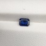 A natural 0.96-carat blue sapphire (Neelam) from Ceylon, Sri Lanka, featuring a faceted oval cut with rich cornflower blue color and high clarity, held securely in professional jeweler's tweezers.