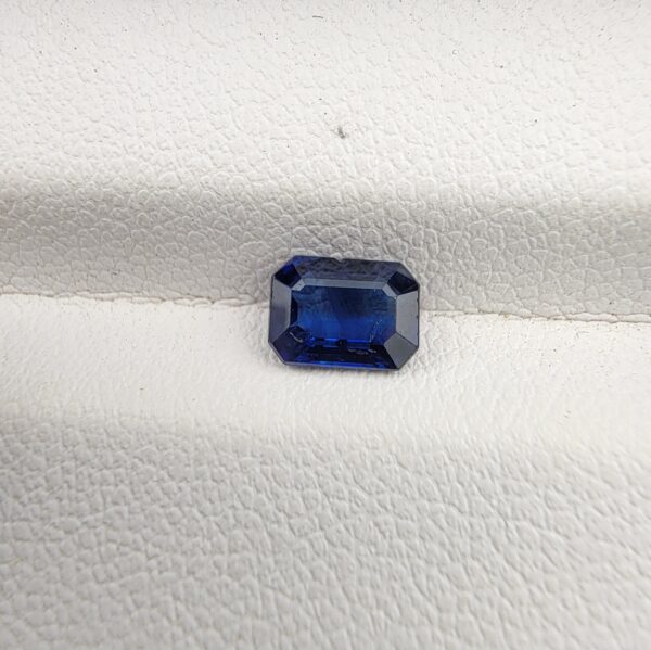 A natural 0.96-carat blue sapphire (Neelam) from Ceylon, Sri Lanka, featuring a faceted oval cut with rich cornflower blue color and high clarity, held securely in professional jeweler's tweezers.