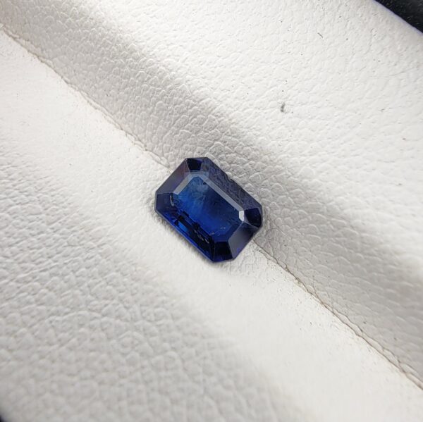 A natural 0.96-carat blue sapphire (Neelam) from Ceylon, Sri Lanka, featuring a faceted oval cut with rich cornflower blue color and high clarity, held securely in professional jeweler's tweezers.