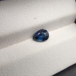 A natural 1.02-carat blue sapphire (Neelam) from Ceylon, Sri Lanka, featuring a masterfully faceted pear shape with brilliant cornflower blue color and a highly transparent crystal structure, held in professional jeweler's tweezers.