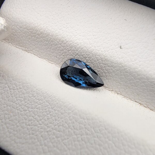 A natural 0.99-carat blue sapphire (Neelam) from Ceylon, Sri Lanka, featuring a masterfully faceted pear shape with brilliant cornflower blue color and a highly transparent crystal structure, resting elegantly on a textured white surface.