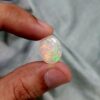 ​A premium 9.73-carat natural Ethiopian oval opal showing an intense, multi-color play-of-color with vibrant flashes of neon green, orange, red, and yellow across its entire dome, held in professional jeweler's tweezers.