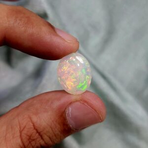 ​A premium 9.73-carat natural Ethiopian oval opal showing an intense, multi-color play-of-color with vibrant flashes of neon green, orange, red, and yellow across its entire dome, held in professional jeweler's tweezers.
