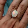 ​A premium 9.73-carat natural Ethiopian oval opal showing an intense, multi-color play-of-color with vibrant flashes of neon green, orange, red, and yellow across its entire dome, held in professional jeweler's tweezers.