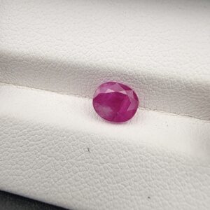 A natural 1.38-carat pinkish-red ruby (Yaqoot) from Mozambique, featuring a faceted oval cut with excellent color saturation and classic internal crystal characteristics, held securely in professional jeweler's tweezers.