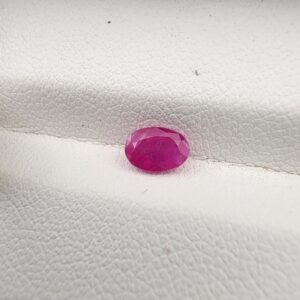 A natural 0.69-carat pinkish-red ruby (Yaqoot) from Mozambique, displaying a faceted oval cut with a distinct translucent crystal structure and natural internal inclusions, resting on a textured white surface.