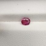 A natural 0.58-carat purple-red ruby (Yaqoot) from Mozambique, displaying a finely faceted oval cut with a completely transparent crystal structure, resting beautifully on a textured white background.