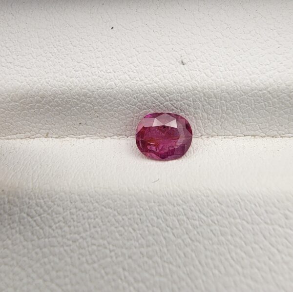 A natural 0.58-carat purple-red ruby (Yaqoot) from Mozambique, displaying a finely faceted oval cut with a completely transparent crystal structure, resting beautifully on a textured white background.