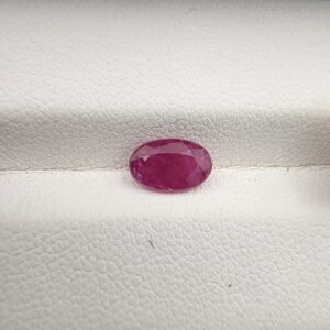 A natural 1.37-carat red ruby (Yaqoot) from Mozambique, displaying a faceted oval cut with a distinct translucent crystal structure and natural internal inclusions, resting on a textured white surface.