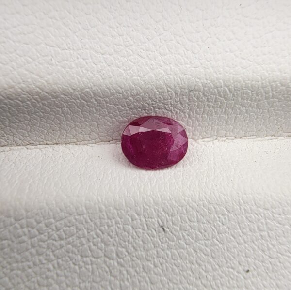 A natural 0.61-carat red ruby (Yaqoot) from Mozambique, displaying a faceted oval cut with a distinct translucent crystal structure and natural internal inclusions, resting on a textured white surface.