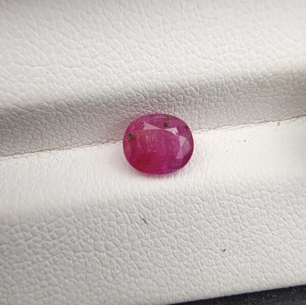 A natural 1.25-carat pinkish-red ruby (Yaqoot) from Mozambique, displaying a faceted oval cut with a distinct semi-transparent crystal structure and noticeable natural internal inclusion markers, resting on a textured white surface.