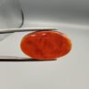 A premium 18.91-carat natural Yemeni Aqeeq agate gemstone with a polished oval cabochon cut, displaying a rich translucent orange-red color profile held securely in professional jeweler's tweezers.