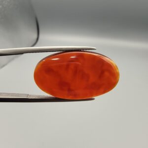 A premium 18.91-carat natural Yemeni Aqeeq agate gemstone with a polished oval cabochon cut, displaying a rich translucent orange-red color profile held securely in professional jeweler's tweezers.