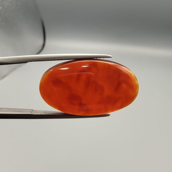 A premium 18.91-carat natural Yemeni Aqeeq agate gemstone with a polished oval cabochon cut, displaying a rich translucent orange-red color profile held securely in professional jeweler's tweezers.