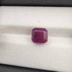 A rare and substantial 5.24-carat purplish-red natural ruby (Yaqoot) from Mozambique, showcasing a premium octagonal step cut with parallel facet lines and a beautiful translucent crystal body, resting on a textured white background.