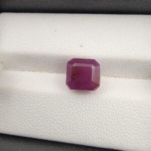 A rare and substantial 5.24-carat purplish-red natural ruby (Yaqoot) from Mozambique, showcasing a premium octagonal step cut with parallel facet lines and a beautiful translucent crystal body, resting on a textured white background.