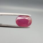 An exceptionally large 6.82-carat natural Mozambican ruby with a premium faceted oval cut, showing a rich translucent purplish-red body color held securely in professional jeweler's tweezers.