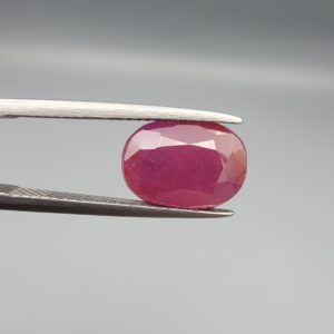 An exceptionally large 6.82-carat natural Mozambican ruby with a premium faceted oval cut, showing a rich translucent purplish-red body color held securely in professional jeweler's tweezers.