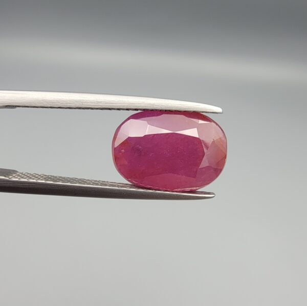 An exceptionally large 6.82-carat natural Mozambican ruby with a premium faceted oval cut, showing a rich translucent purplish-red body color held securely in professional jeweler's tweezers.