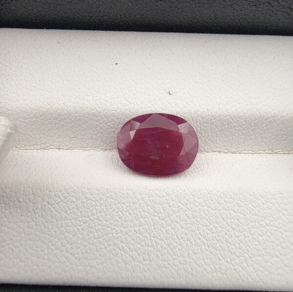 A premium 3.24-carat natural, unheated Mozambican ruby showing a faceted oval shape with a deep purplish-red translucent color profile, resting inside a textured white leather jewelry box liner.