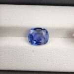 ​A premium 3.98-carat natural Ceylon blue sapphire gemstone displaying an elegant cushion cut with excellent symmetry and a deep royal blue color profile, resting inside a textured white leather jewelry box liner.