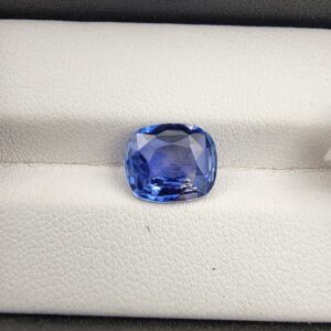 ​A premium 3.98-carat natural Ceylon blue sapphire gemstone displaying an elegant cushion cut with excellent symmetry and a deep royal blue color profile, resting inside a textured white leather jewelry box liner.