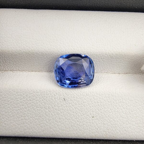 ​A premium 3.98-carat natural Ceylon blue sapphire gemstone displaying an elegant cushion cut with excellent symmetry and a deep royal blue color profile, resting inside a textured white leather jewelry box liner.