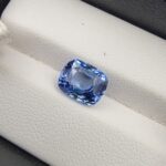 A premium 4.07-carat natural Ceylon blue sapphire gemstone displaying an elegant cushion cut with excellent symmetry and a deep royal blue color profile, resting inside a textured white leather jewelry box liner.