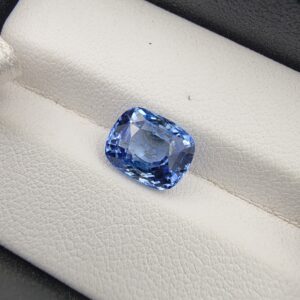 A premium 4.07-carat natural Ceylon blue sapphire gemstone displaying an elegant cushion cut with excellent symmetry and a deep royal blue color profile, resting inside a textured white leather jewelry box liner.