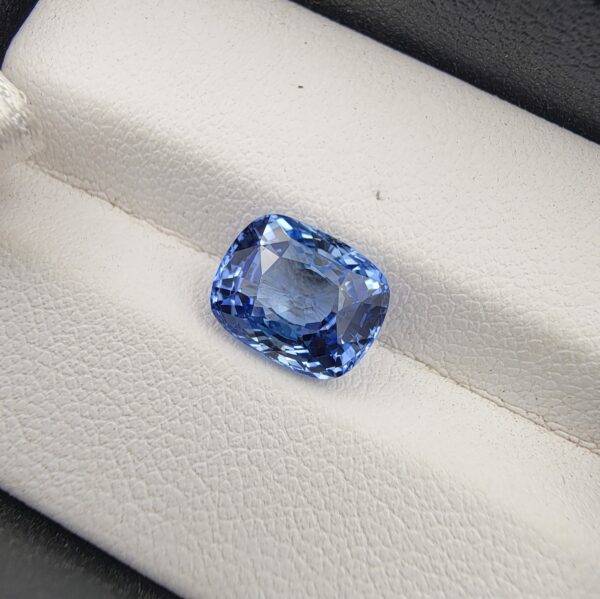 A premium 4.07-carat natural Ceylon blue sapphire gemstone displaying an elegant cushion cut with excellent symmetry and a deep royal blue color profile, resting inside a textured white leather jewelry box liner.