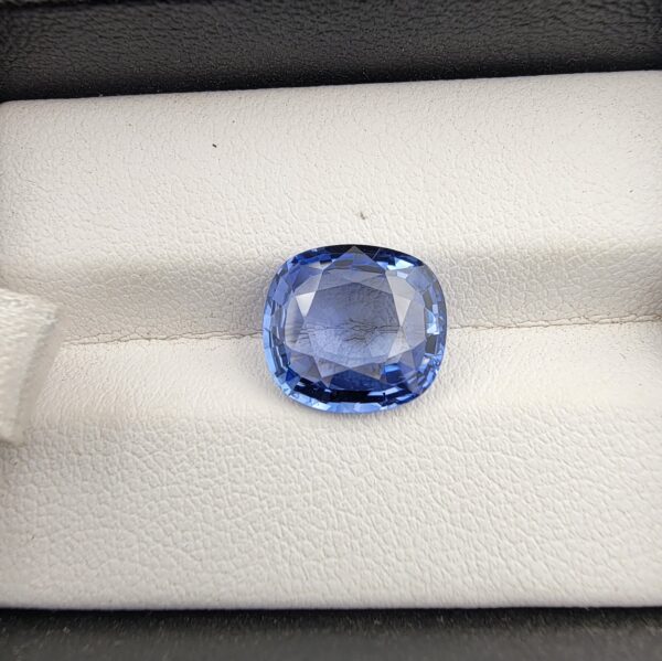 A premium 5.15-carat natural Ceylon blue sapphire gemstone displaying an elegant cushion cut with excellent symmetry and a deep royal blue color profile, resting inside a textured white leather jewelry box liner.