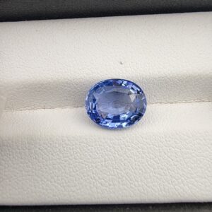 ​A premium 4.40-carat natural Ceylon blue sapphire gemstone displaying an elegant oval cut with excellent symmetry and a deep royal blue color profile, resting inside a textured white leather jewelry box liner.