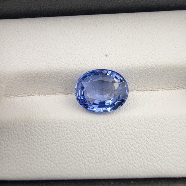 ​A premium 4.40-carat natural Ceylon blue sapphire gemstone displaying an elegant oval cut with excellent symmetry and a deep royal blue color profile, resting inside a textured white leather jewelry box liner.