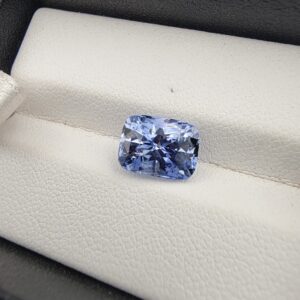 ​A premium 3.67-carat natural Ceylon blue sapphire gemstone displaying an elegant cushion cut with excellent symmetry and a deep royal blue color profile, resting inside a textured white leather jewelry box liner.
