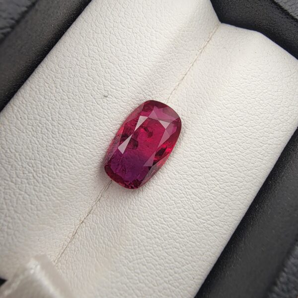 A premium 4.02-carat natural Mozambique ruby gemstone held horizontally by jeweler's tweezers, showcasing an elegant elongated cushion cut, vibrant purplish-red body color, and stunning transparent clarity with distinct internal crystal inclusions.