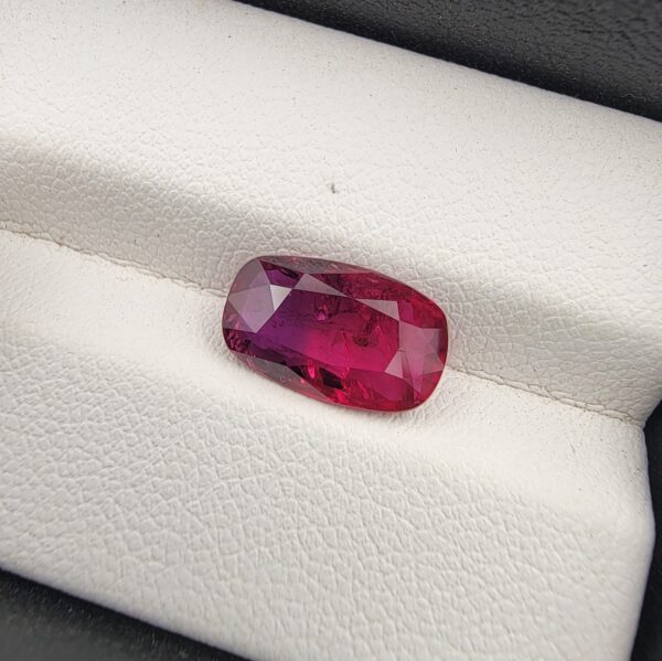A premium 4.02-carat natural Mozambique ruby gemstone held horizontally by jeweler's tweezers, showcasing an elegant elongated cushion cut, vibrant purplish-red body color, and stunning transparent clarity with distinct internal crystal inclusions.