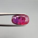A premium 4.02-carat natural Mozambique ruby gemstone held horizontally by jeweler's tweezers, showcasing an elegant elongated cushion cut, vibrant purplish-red body color, and stunning transparent clarity with distinct internal crystal inclusions.