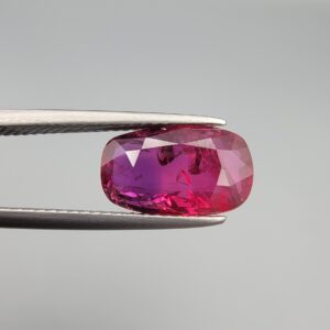 A premium 4.02-carat natural Mozambique ruby gemstone held horizontally by jeweler's tweezers, showcasing an elegant elongated cushion cut, vibrant purplish-red body color, and stunning transparent clarity with distinct internal crystal inclusions.